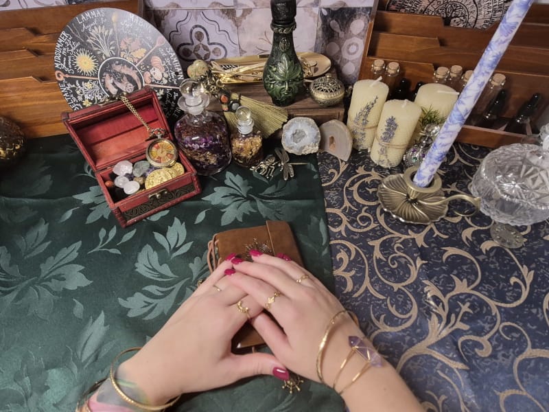 Spiritual reading altar with hands, tarot deck, crystals, candles, and ritual tools