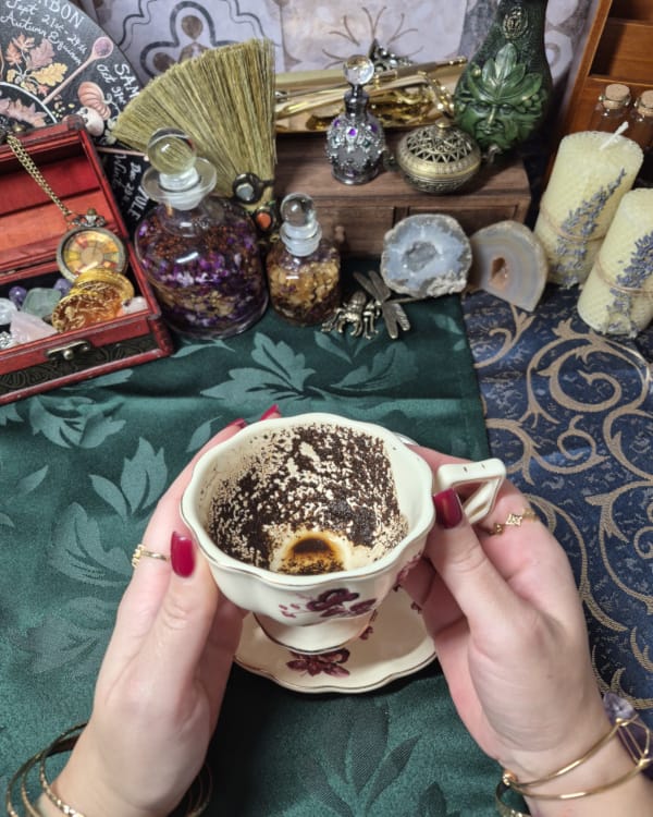 Coffee reading with cup held over ritual table and spiritual tools